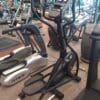 A black elliptical machine with a digital console stands in a gym among treadmills and stationary bikes.