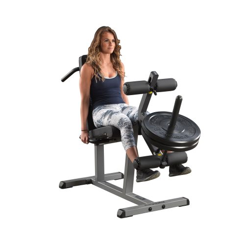 A woman in a navy tank top and leggings uses a seated leg extension machine with weights against a plain white background.