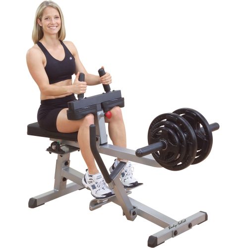 A woman in black workout attire uses a seated calf raise machine, pressing with her legs against weight-loaded resistance.